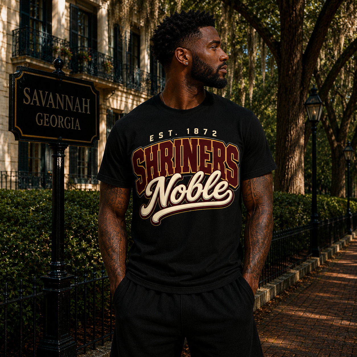 Model wearing the Shriners Noble black T-shirt with maroon, cream, and gold collegiate graphic