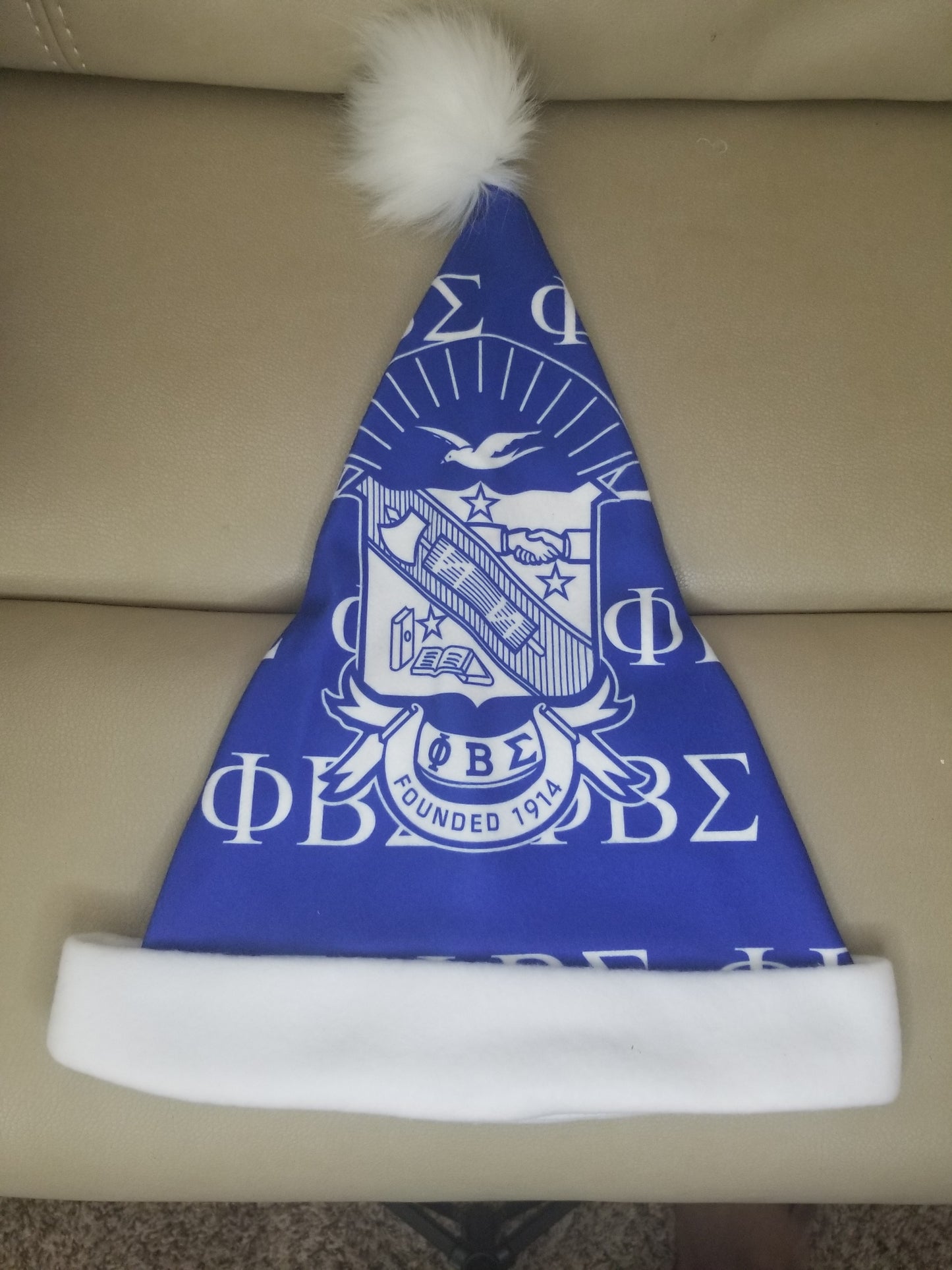 A blue and white Phi Beta Sigma Santa hat with a white pom-pom on top, featuring the fraternity's logo and initials.
