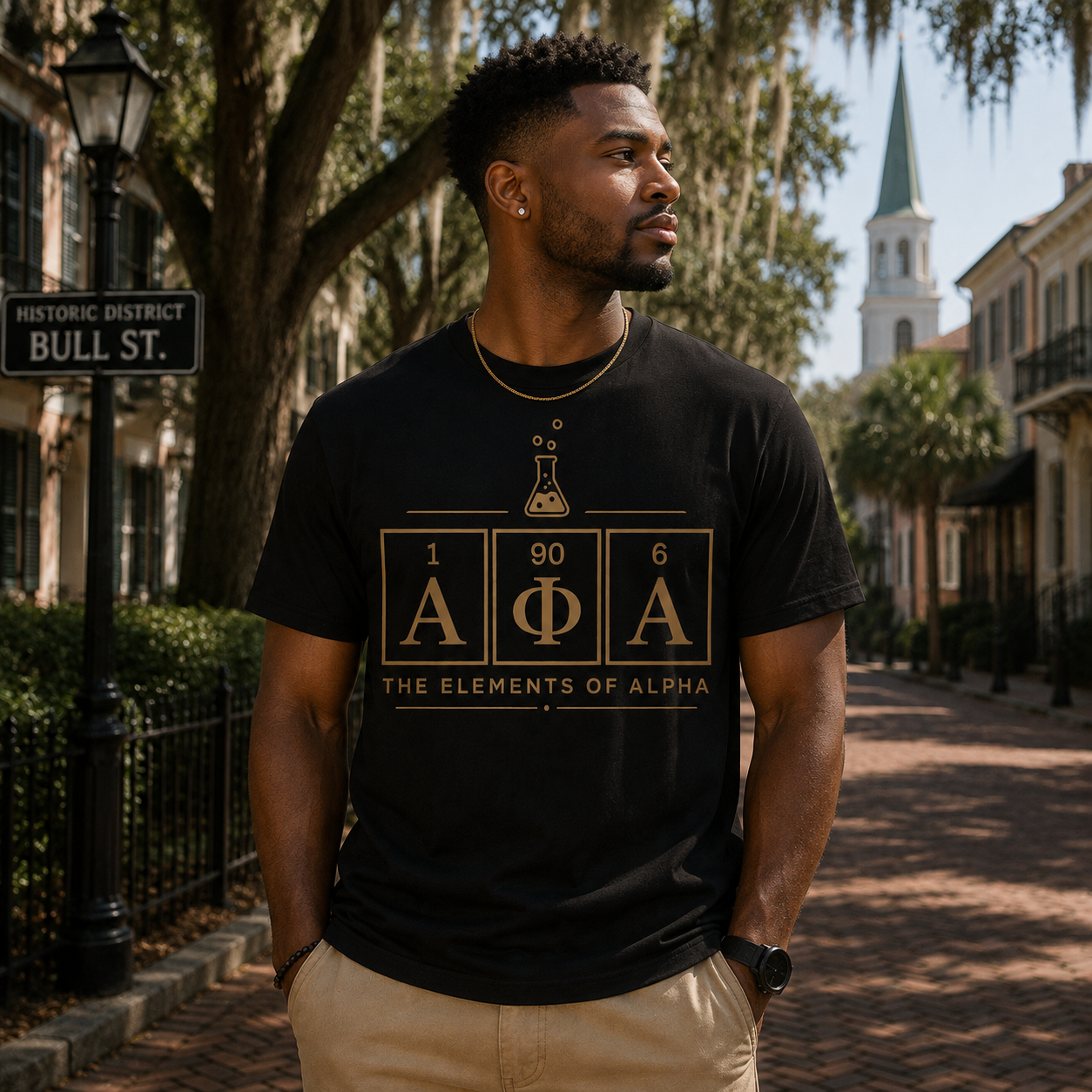 Model wearing the Alpha Phi Alpha Elements of Alpha black T-shirt with gold chemistry graphic