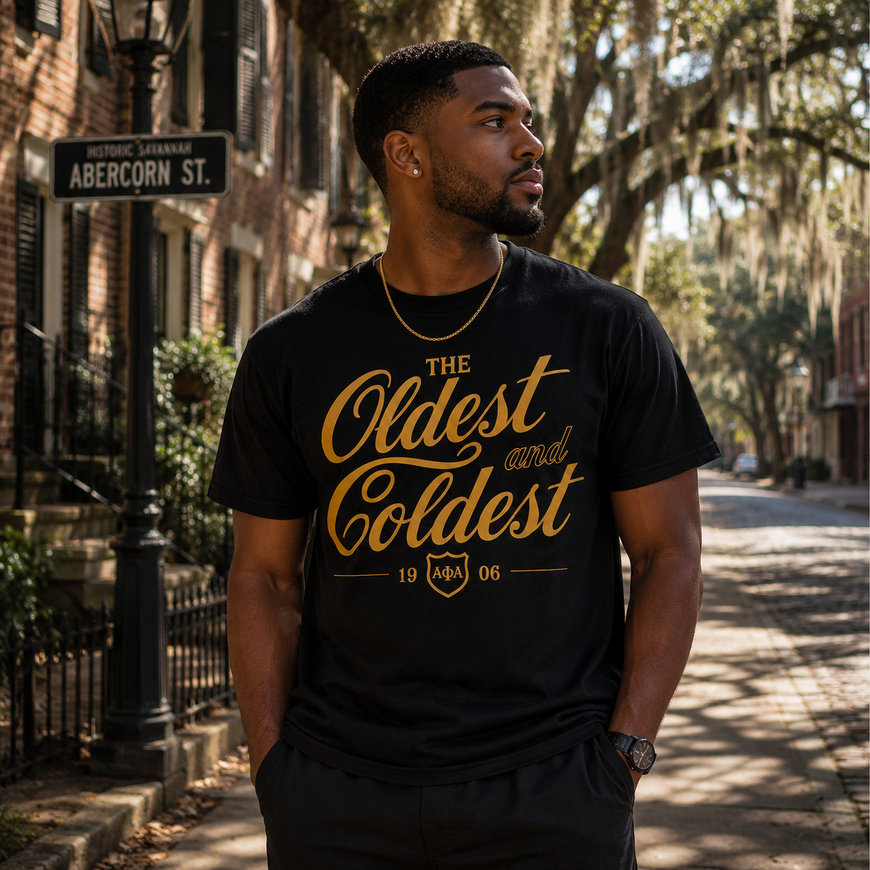 Model wearing the Alpha Phi Alpha Oldest and Coldest black T-shirt with gold script graphic