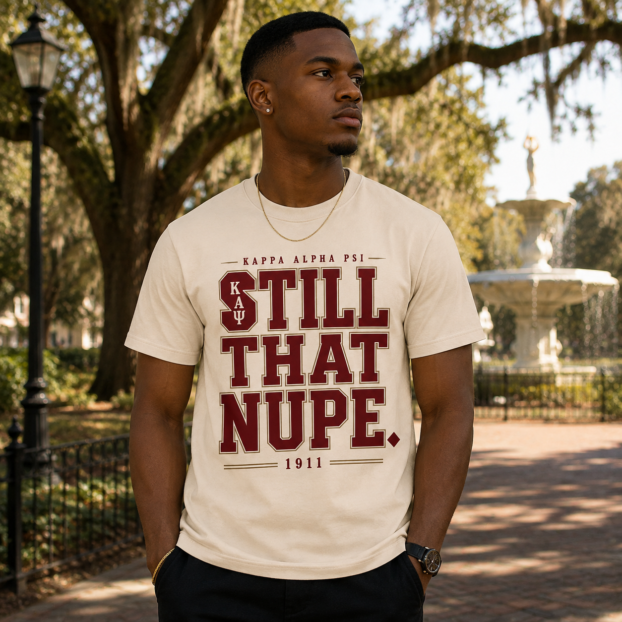 Model wearing the Kappa Alpha Psi Still That Nupe cream T-shirt with crimson and gold collegiate graphic