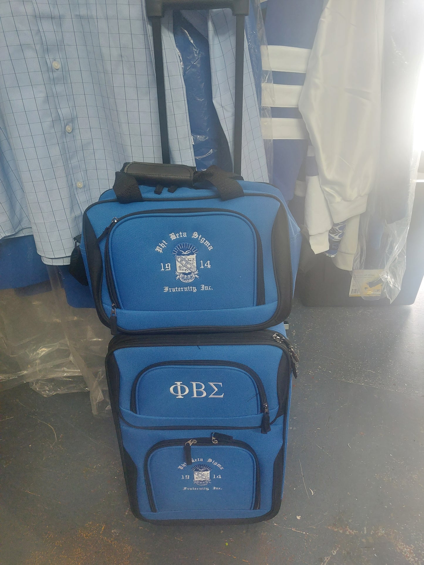 A blue 2-piece expandable carry-on luggage set with Greek letters printed on the bags, upright position, with a retractable handle and four wheels visible.
