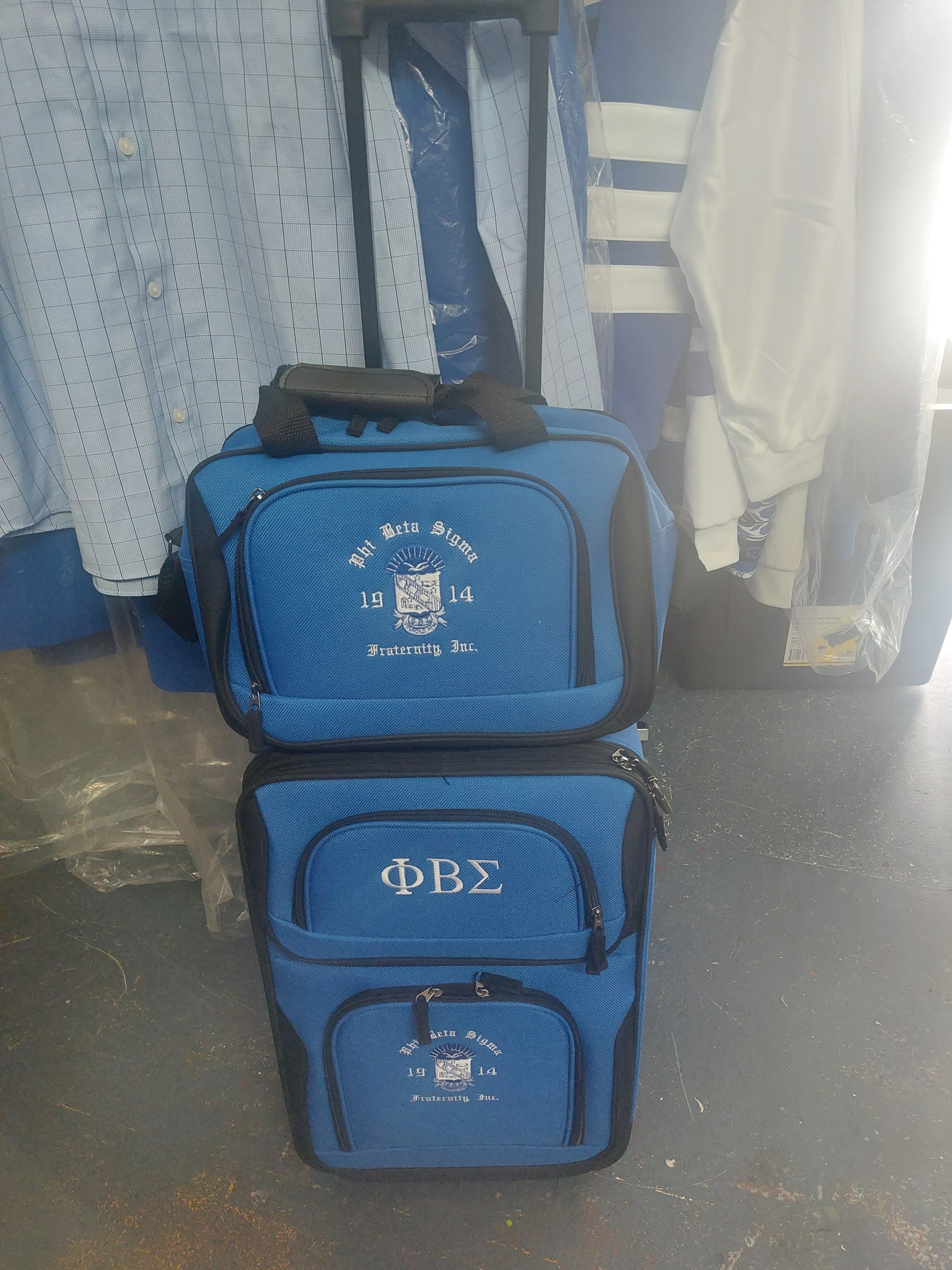 A blue 2-piece expandable carry-on luggage set with Greek letters printed on the bags, upright position, with a retractable handle and four wheels visible.