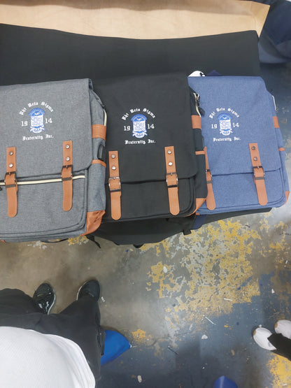 A collection of Phi Beta Sigma backpacks in black and blue colors, featuring leather accents and a logo on the front.