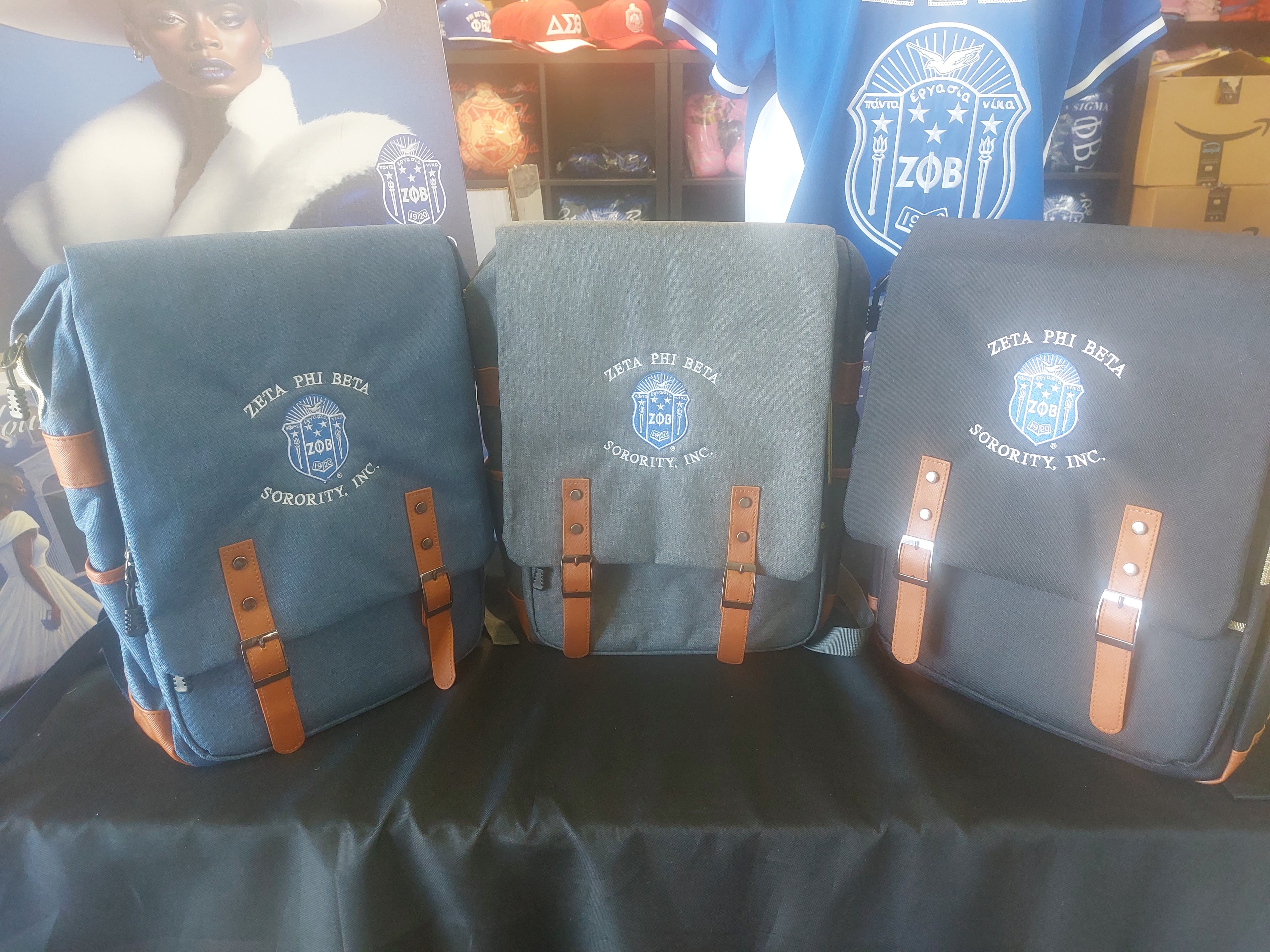 A collection of Zeta Phi Beta backpacks displayed on a table, featuring a compartment for laptops and other storage pockets, with leather straps and a structured design.