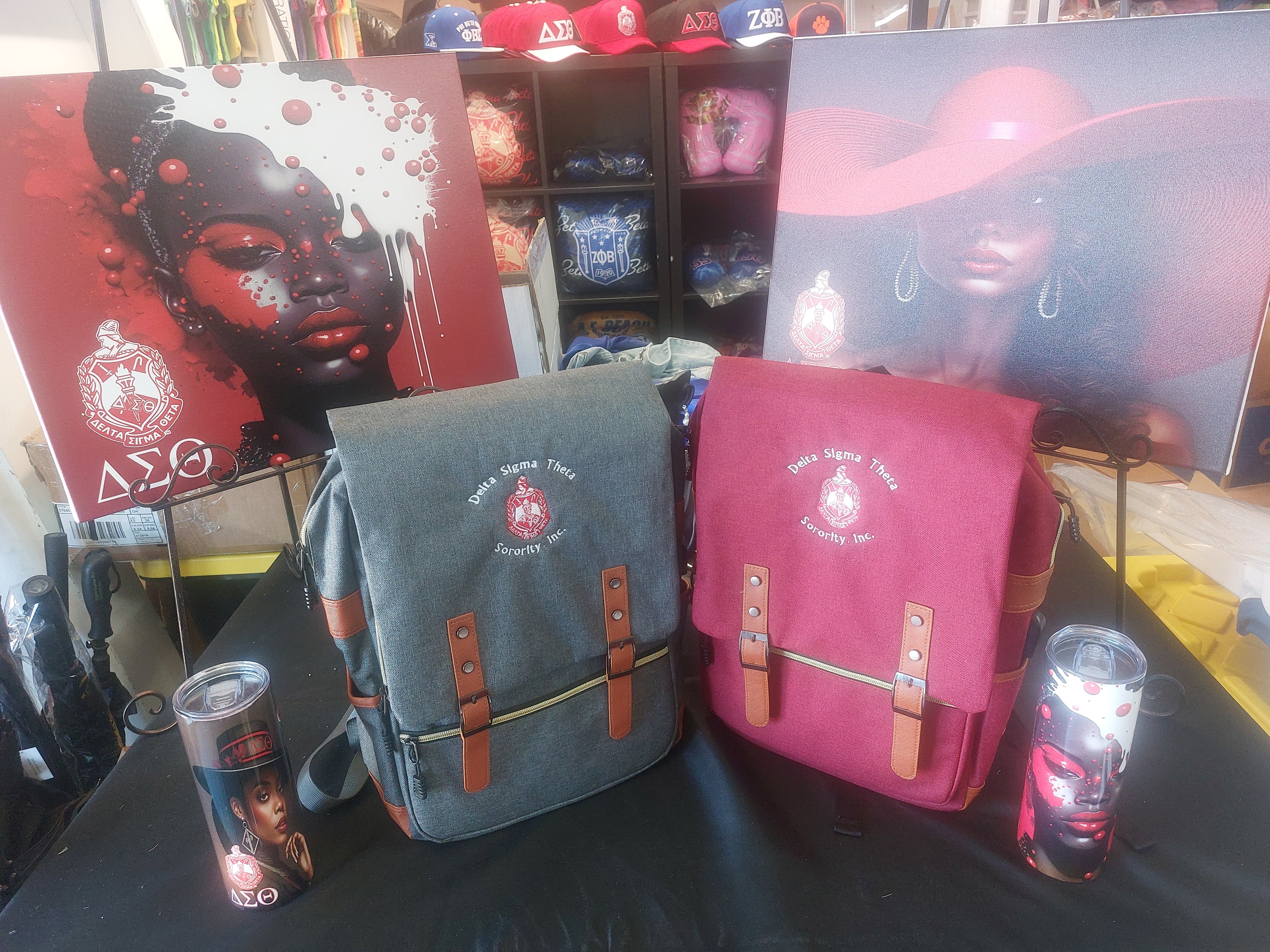 Two Delta Sigma Theta backpacks, one gray and one red, displayed with a graphic design and a candle on a table.