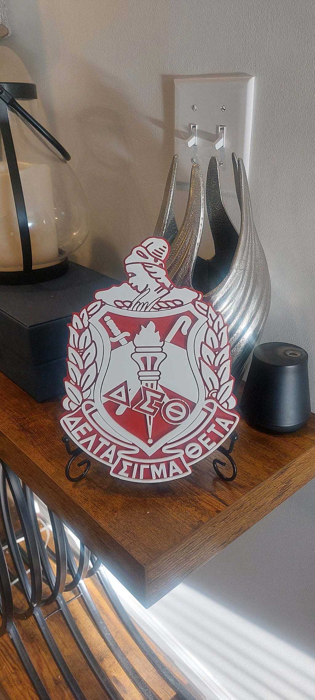 A Delta Sigma Theta 3D Shield with a red and white color scheme, featuring intricate details and a 3D effect, displayed on a wooden surface.