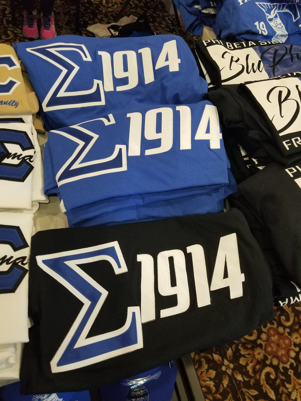 A collection of Phi Beta Sigma shirts displayed, featuring the organization's symbols and the year 1914.