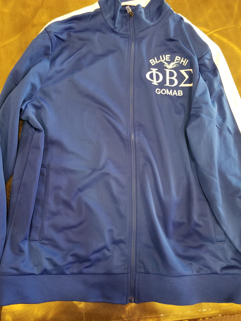 A blue Phi Beta Sigma track jacket with white stripe accents and the fraternity's logo on the back.
