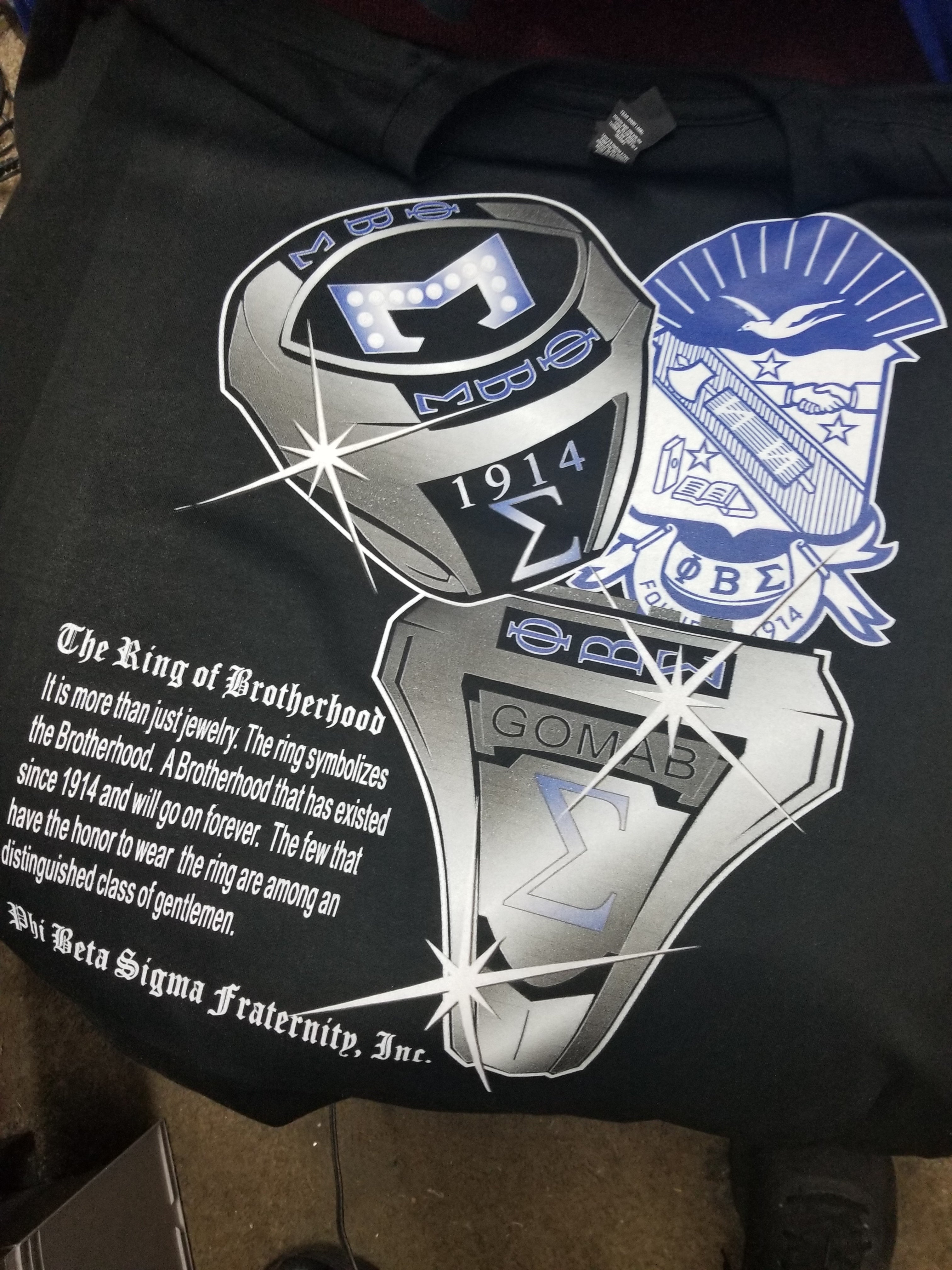 A black Phi Beta Sigma Fraternity ring shirt with white and blue text and emblems.