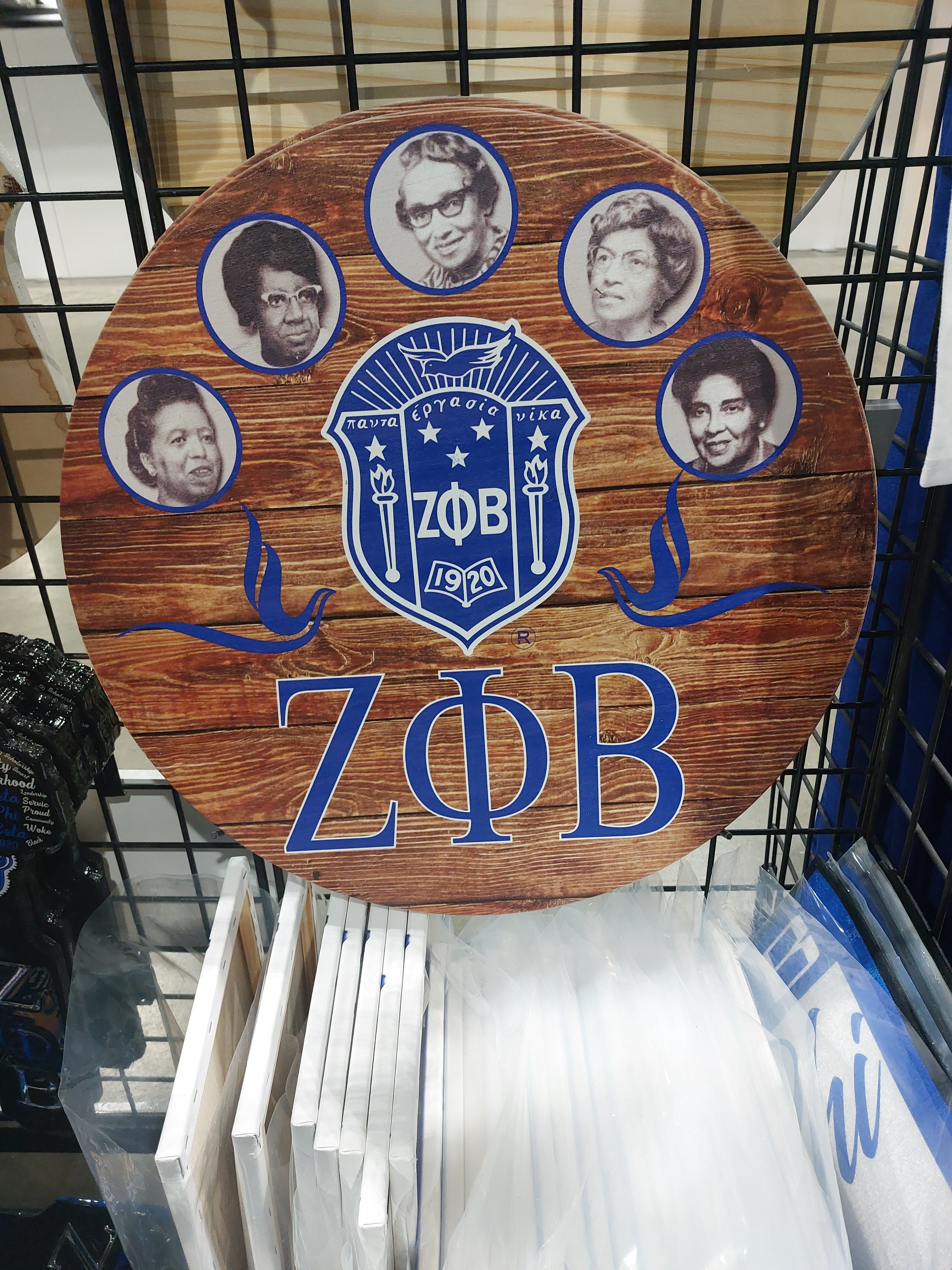 A round wooden plaque with a Zeta Phi Beta logo in blue and white, featuring photographs of individuals in the center.