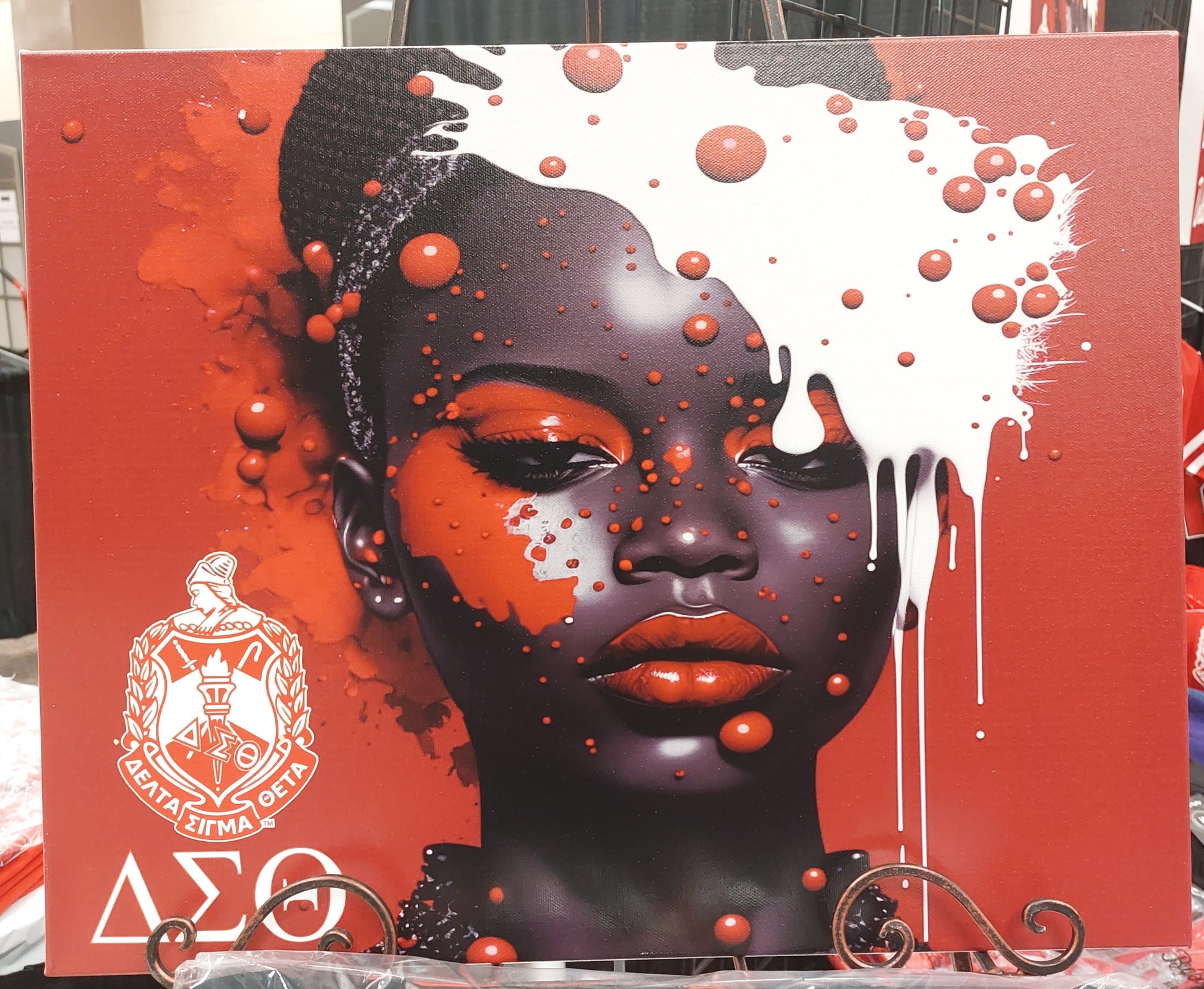 A canvas wall art featuring the Delta Sigma Theta sorority symbol with Greek letters, predominantly red and black with a splash of white paint, mounted on a wooden frame.