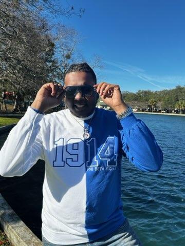 A person standing by a body of water, wearing a split sweatshirt with one half white and the other blue, with the numbers 1914 printed on the white half.