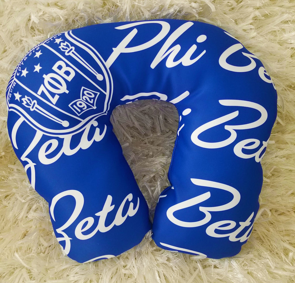 A blue neck pillow with the Zeta Phi Beta fraternity logo printed on it, displayed on a white fuzzy surface.